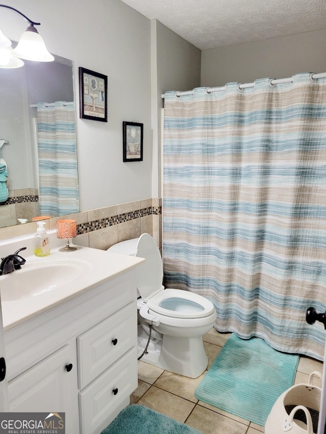 full bath featuring vanity, tile patterned flooring, a textured ceiling, tile walls, and toilet