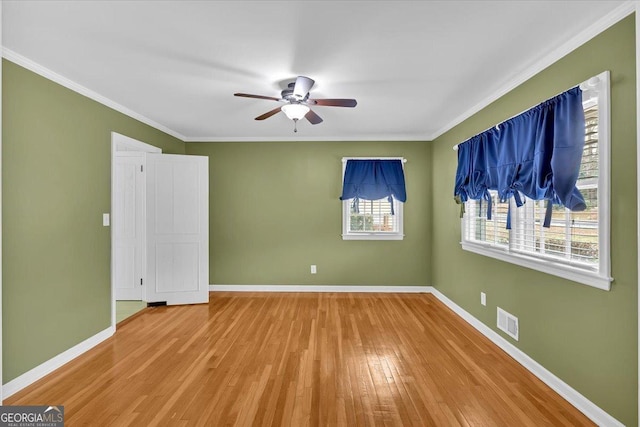 spare room featuring visible vents, baseboards, ornamental molding, wood finished floors, and a ceiling fan