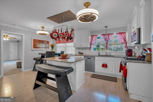 kitchen with a sink, appliances with stainless steel finishes, ornamental molding, and white cabinetry