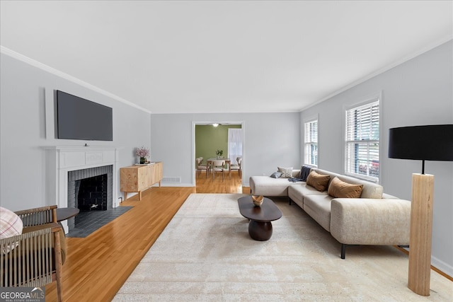 living area with visible vents, crown molding, baseboards, a fireplace, and light wood-style floors