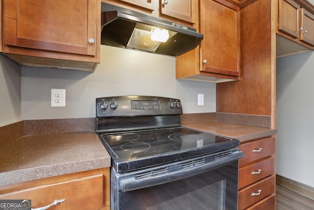 kitchen featuring brown cabinets, under cabinet range hood, black electric range, dark countertops, and wood finished floors