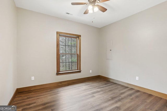 spare room featuring visible vents, a ceiling fan, electric panel, wood finished floors, and baseboards