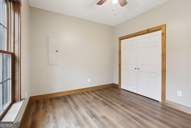 unfurnished bedroom featuring electric panel, wood finished floors, a closet, baseboards, and ceiling fan