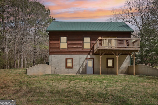 back of property at dusk with a wooden deck, a yard, faux log siding, brick siding, and metal roof