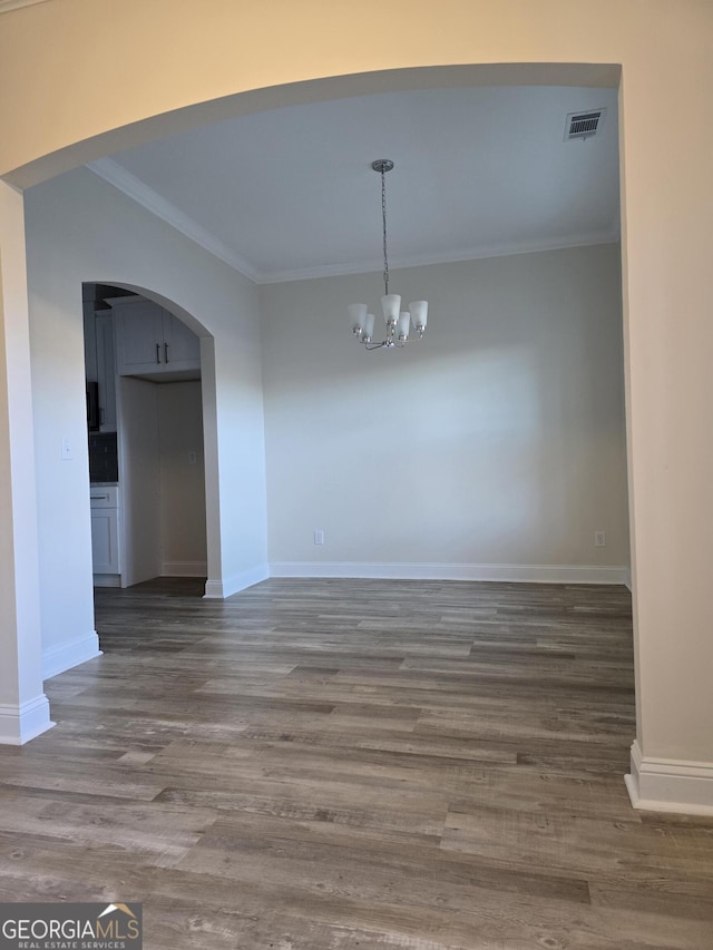 unfurnished dining area with crown molding, baseboards, wood finished floors, arched walkways, and a notable chandelier