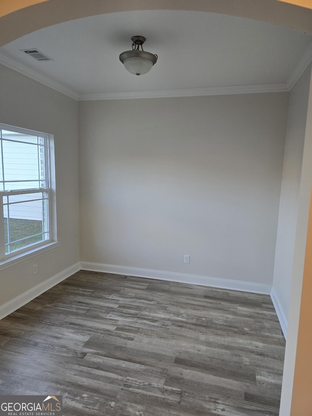 empty room with visible vents, baseboards, wood finished floors, and crown molding