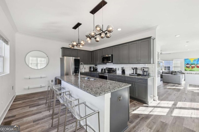 kitchen featuring a sink, backsplash, stainless steel appliances, an inviting chandelier, and light stone countertops