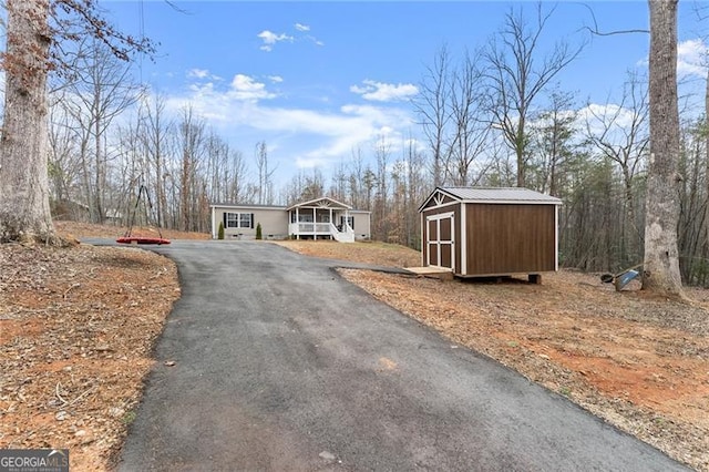 view of front of house with aphalt driveway, an outbuilding, a storage shed, and metal roof
