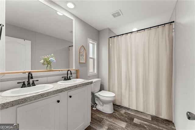full bath featuring toilet, wood finished floors, visible vents, and a sink