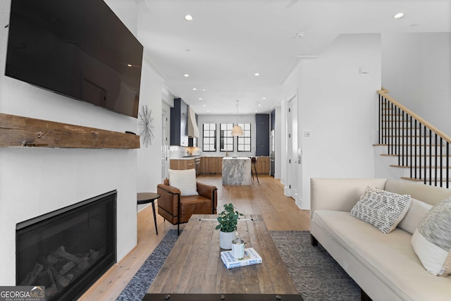 living room featuring a glass covered fireplace, stairs, recessed lighting, and light wood finished floors