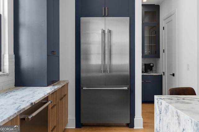 kitchen featuring tasteful backsplash, light stone counters, stainless steel appliances, blue cabinets, and light wood-type flooring