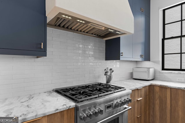 kitchen with backsplash, light stone countertops, high end stainless steel range, and premium range hood