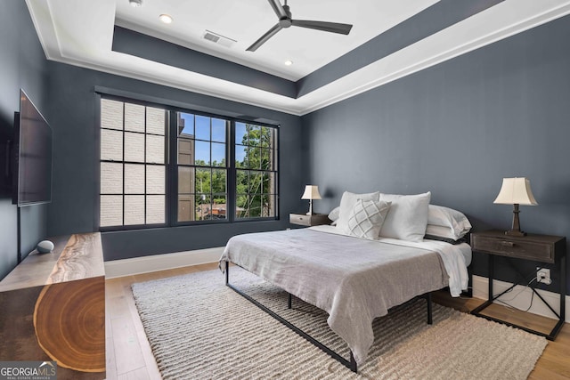 bedroom featuring a tray ceiling, wood finished floors, visible vents, and baseboards