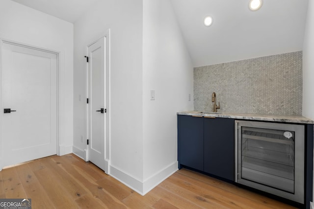 bar featuring wine cooler, light wood finished floors, indoor wet bar, and a sink