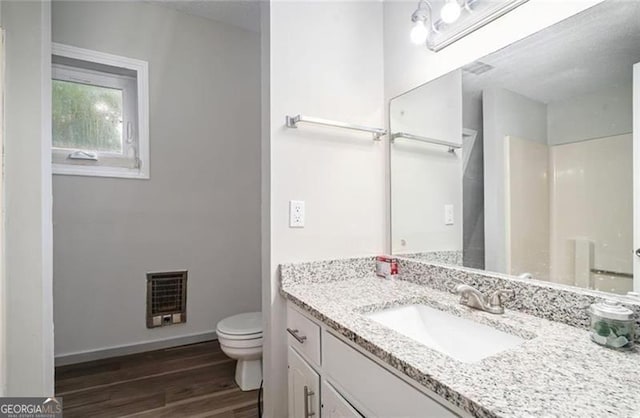 bathroom with toilet, heating unit, wood finished floors, baseboards, and vanity