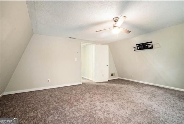 empty room featuring lofted ceiling, a ceiling fan, a textured ceiling, carpet floors, and baseboards