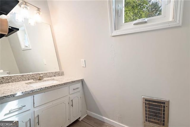 bathroom with baseboards, heating unit, wood finished floors, and vanity