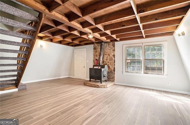 unfurnished living room featuring stairway, baseboards, wood finished floors, and a wood stove