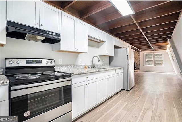 kitchen featuring freestanding refrigerator, a sink, electric stove, under cabinet range hood, and white cabinetry