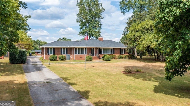 ranch-style home featuring aphalt driveway, brick siding, a front yard, and a chimney