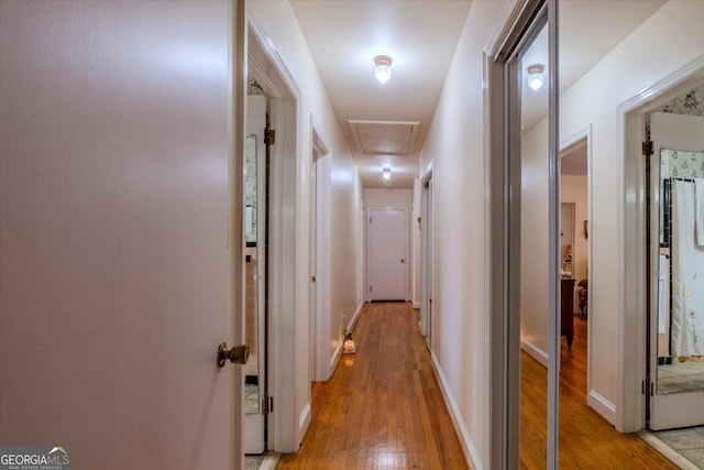 hall with attic access, light wood-style flooring, and baseboards