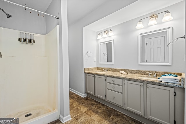 bathroom featuring a sink, baseboards, a stall shower, and double vanity