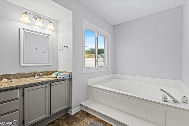 bathroom with a tub with jets, vanity, and baseboards