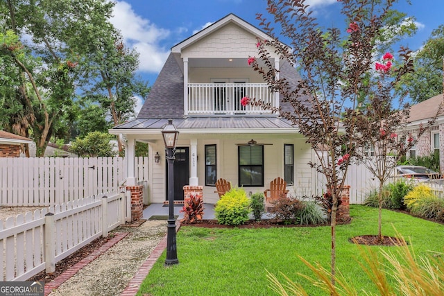 view of front of home featuring a front yard, a balcony, fence, a porch, and metal roof