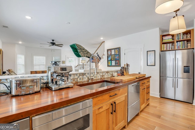 kitchen with a sink, light wood-style floors, appliances with stainless steel finishes, butcher block counters, and ceiling fan