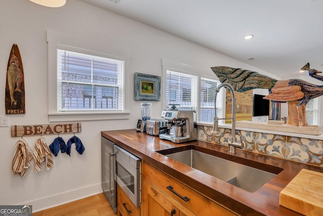 kitchen featuring baseboards, light wood finished floors, a sink, butcher block countertops, and stainless steel microwave