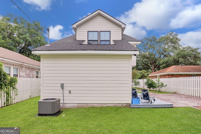 back of property featuring a lawn, cooling unit, a shingled roof, and a fenced backyard