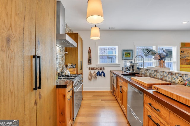 kitchen with visible vents, a sink, stainless steel appliances, wall chimney range hood, and light wood-type flooring