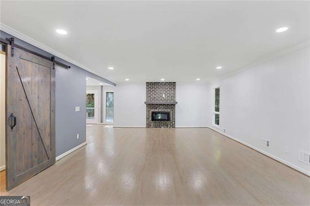 unfurnished living room with a barn door, a brick fireplace, recessed lighting, and light wood-style floors