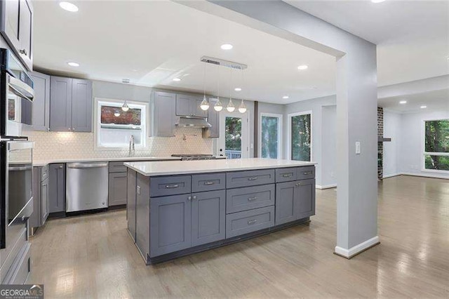 kitchen with gray cabinets, under cabinet range hood, tasteful backsplash, stainless steel appliances, and light wood-style floors