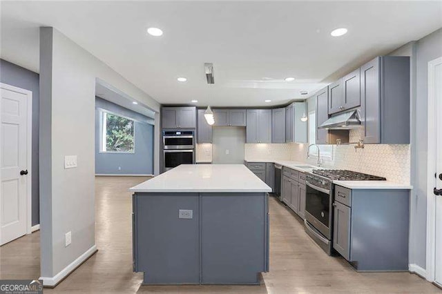 kitchen with under cabinet range hood, gray cabinetry, stainless steel appliances, and a sink