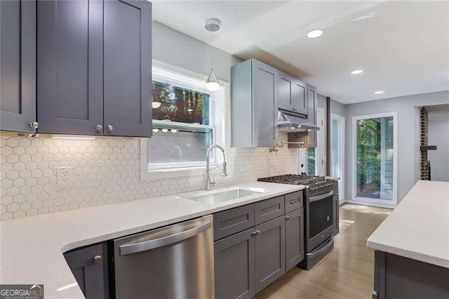 kitchen with under cabinet range hood, light countertops, appliances with stainless steel finishes, hanging light fixtures, and a sink