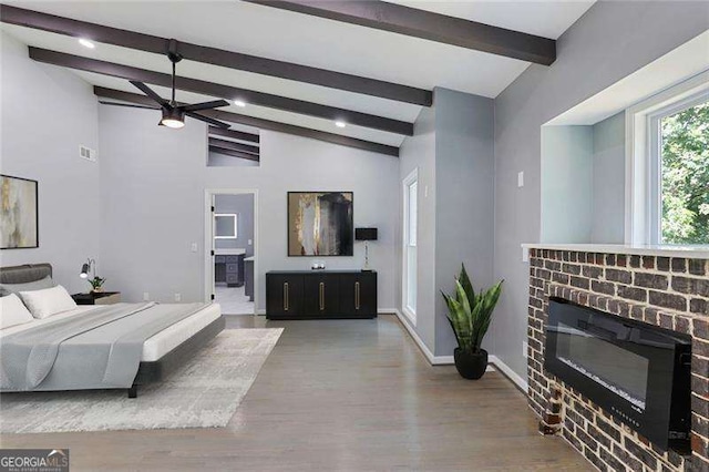 bedroom with lofted ceiling with beams, wood finished floors, a fireplace, and baseboards