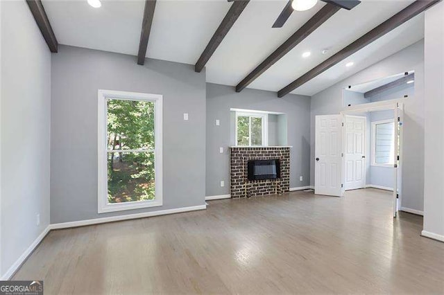 unfurnished living room with lofted ceiling with beams, baseboards, a brick fireplace, and wood finished floors