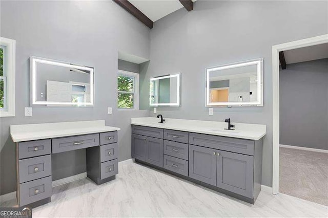 full bath with double vanity, beamed ceiling, baseboards, and a sink