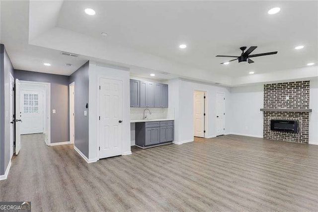 unfurnished living room with wood finished floors, a fireplace, ceiling fan, a sink, and a raised ceiling