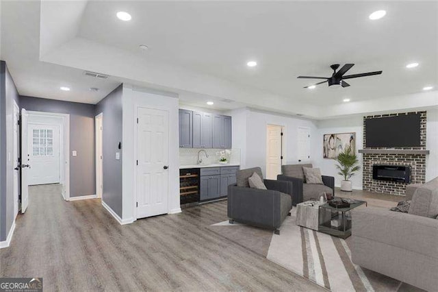 living room featuring a brick fireplace, a ceiling fan, a raised ceiling, and light wood-style floors