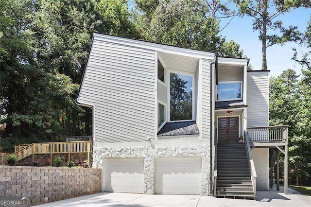 view of front facade with stone siding, french doors, concrete driveway, an attached garage, and stairs