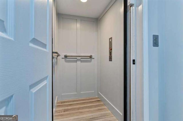 hallway with elevator and light wood-style floors