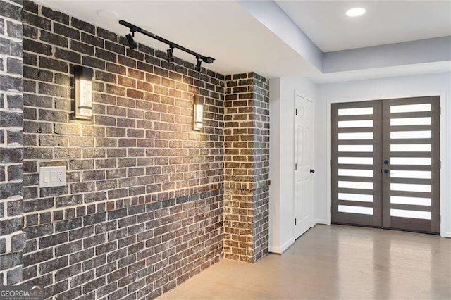 foyer entrance featuring brick wall, baseboards, rail lighting, and french doors