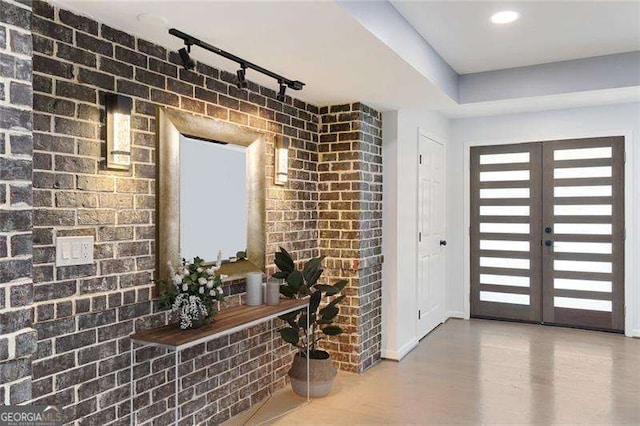 foyer entrance featuring track lighting, brick wall, french doors, and wood finished floors