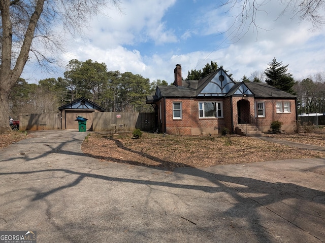 view of front facade featuring fence, brick siding, driveway, and a chimney