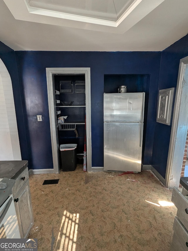 interior space featuring visible vents, baseboards, carpet, freestanding refrigerator, and a raised ceiling