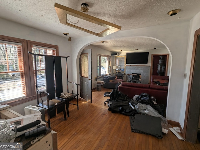 living area with arched walkways, a fireplace, a textured ceiling, and hardwood / wood-style floors