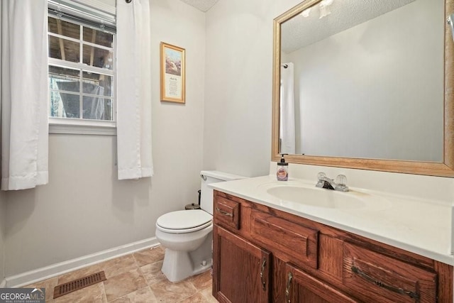 bathroom featuring toilet, vanity, a textured ceiling, visible vents, and baseboards