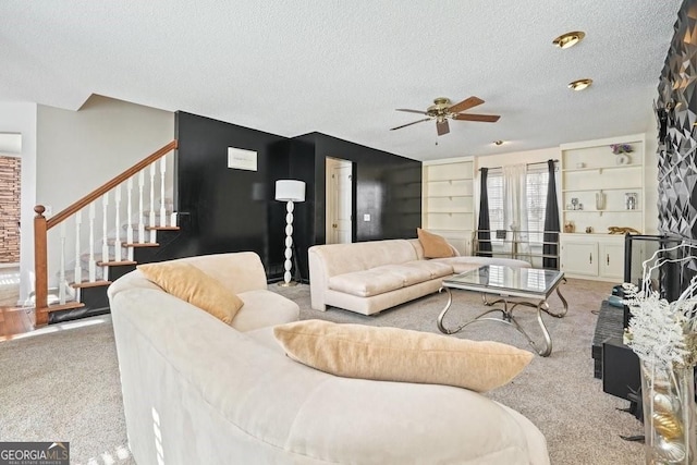 carpeted living area featuring ceiling fan, stairs, a textured ceiling, and built in shelves